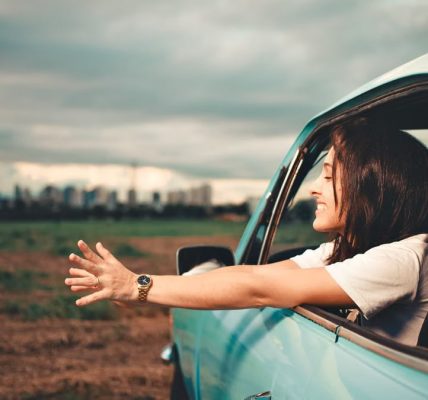 Woman enjoying the fresh air while leaning out of a blue car window on a road trip.
