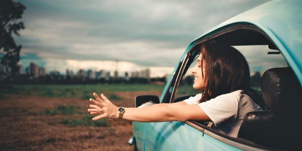 Woman enjoying the fresh air while leaning out of a blue car window on a road trip.