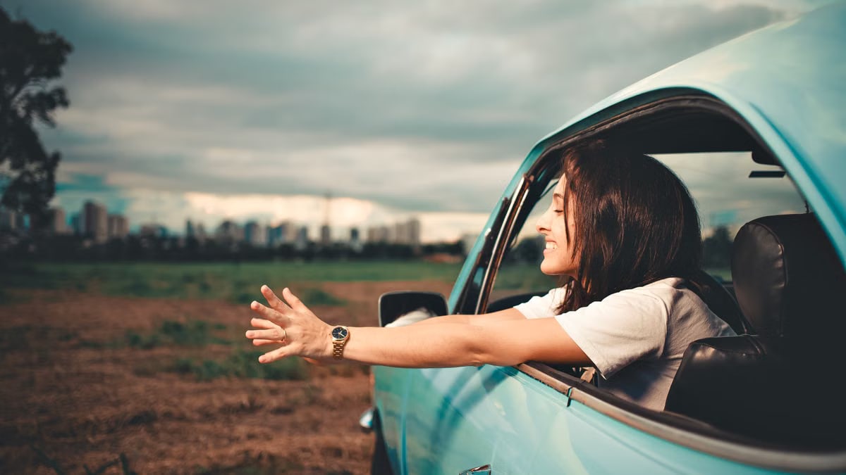 Woman enjoying the fresh air while leaning out of a blue car window on a road trip.